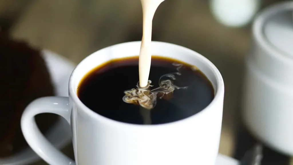 Milch wird in eine Tasse Kaffee gegossen