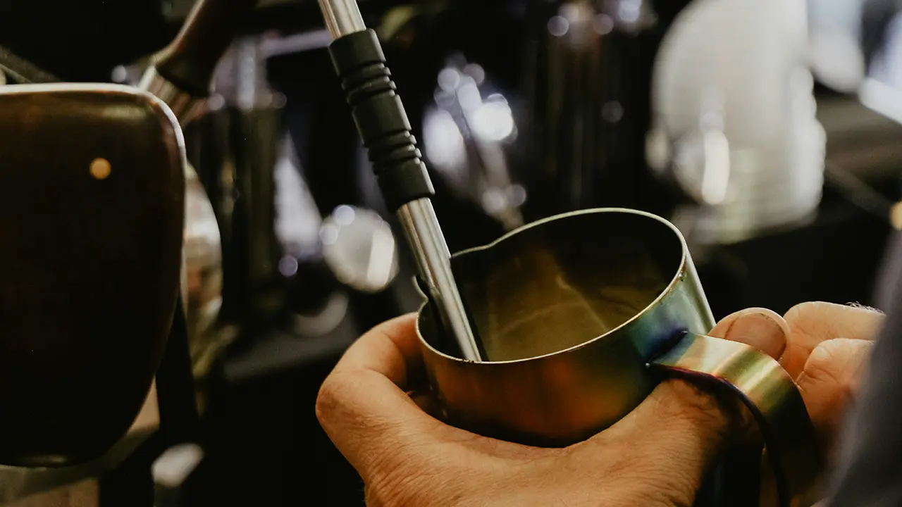 Ein Hand hält ein Milchkännchen unter eine Dampfpflanze